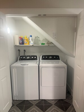 A laundry room with two front-loading washing machines and a shelf above containing cleaning supplies. - NEW! Brickhouse Villas. 2 blocks from UF. Early check in/late check out. Parking (gainesville)