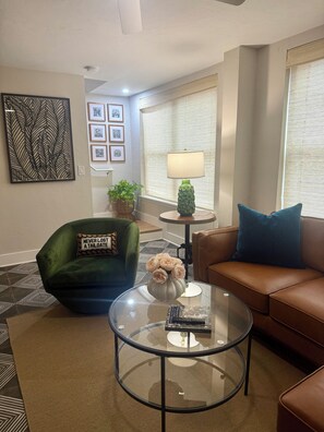 A living room with a green chair, a brown sofa, a glass coffee table, a lamp, and a vase with flowers. - NEW! Brickhouse Villas. 2 blocks from UF. Early check in/late check out. Parking (gainesville)