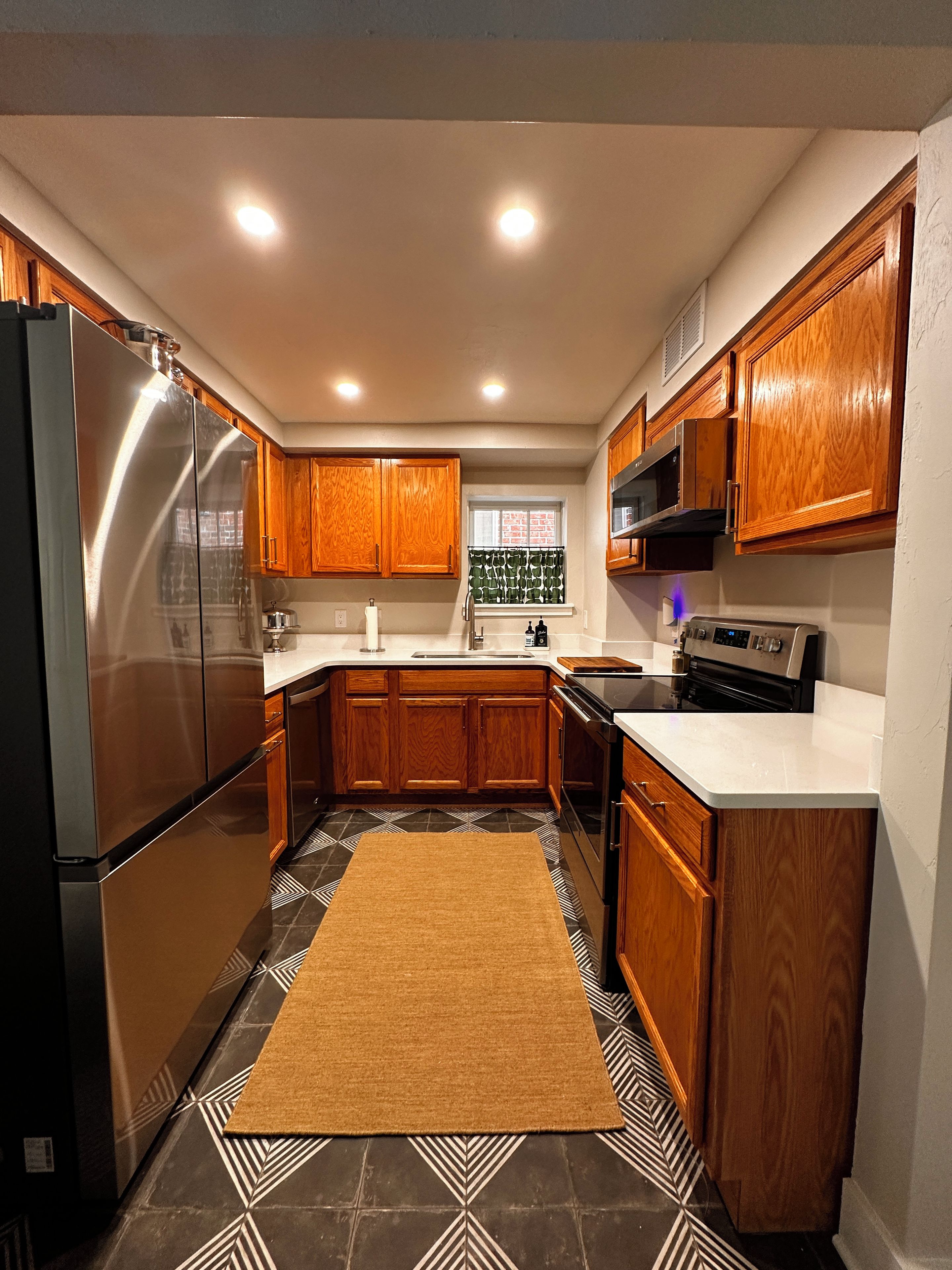 A modern kitchen with stainless steel appliances, wooden cabinets, and a patterned floor.