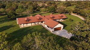 A large, single-story house with a red roof, a covered patio, and a driveway leading to a garage. - The Limestone Retreat at Ruby Ranch Getaways (Buda)