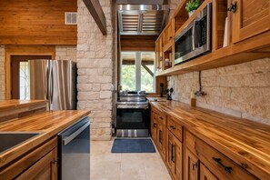 A modern kitchen with wooden cabinets, stainless steel appliances, and a stone accent wall. - The Limestone Retreat at Ruby Ranch Getaways (Buda)