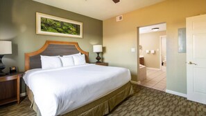 A hotel room with a large bed, a nightstand with a lamp, a framed picture on the wall, and a bathroom visible through an open door. - Uncover Family Fun and Mountain Adventure at Wyndham Smoky Mountains – 2 Bd. Dlx (Sevierville)