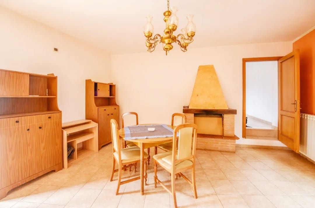 Een kamer met een eettafel, stoelen, een kroonluchter, houten kasten en een open haard.