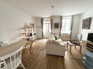 Ein Wohnzimmer mit einer Couch, einem Esstisch, einem Fernseher und einem Bücherregal.