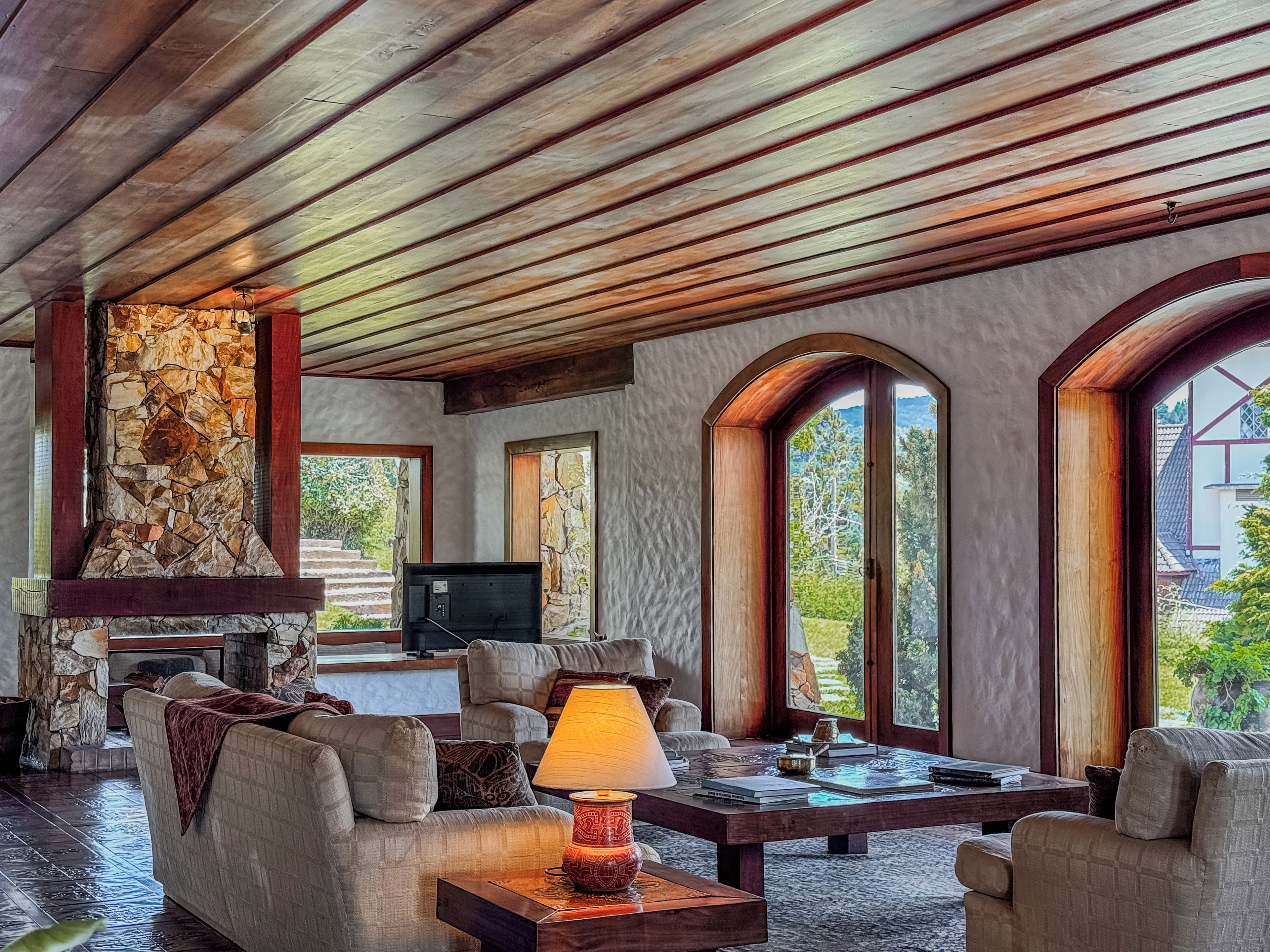 Uma sala de estar ampla com lareira de pedra, assentos confortáveis e grandes janelas com vista para o exterior.