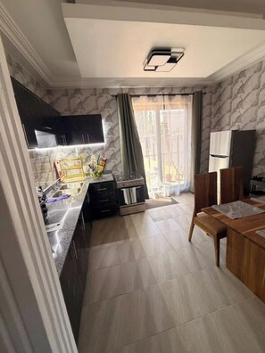 A kitchen with a built-in oven, a dining table, and a window with curtains. - Soronko Sanctuary. A cozy & whimsical city apt! Gated, 24/7 security, A/C, + (Dome)