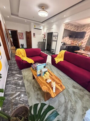 Un salon moderne avec deux canapés rouges, une table basse en bois et une cuisine en arrière-plan.