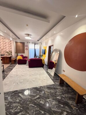 A modern hotel lobby with a marble floor, red sofas, a wooden bench, a large mirror, and a TV on the wall. - Soronko Sanctuary. A cozy & whimsical city apt! Gated, 24/7 security, A/C, + (Dome)