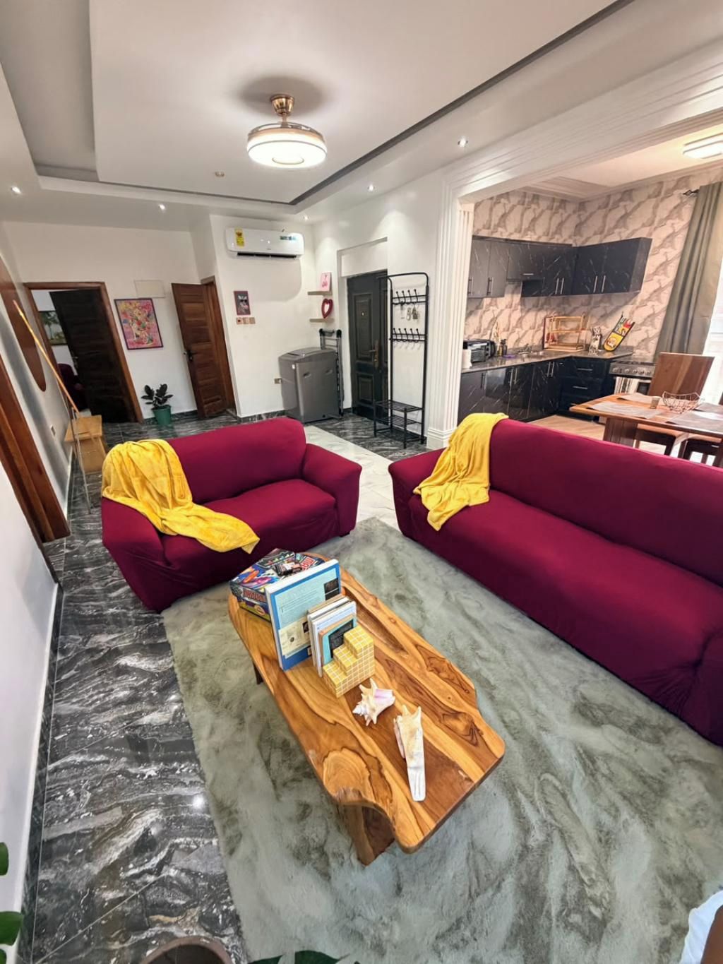 A living room with two red sofas, a wooden coffee table, and a kitchen in the background.