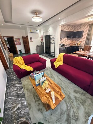 A living room with two red sofas, a wooden coffee table, and a kitchen in the background. - Soronko Sanctuary. A cozy & whimsical city apt! Gated, 24/7 security, A/C, + (Dome)