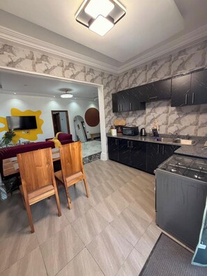 A modern kitchen with dark cabinets, a built-in stove, and a dining area with wooden chairs and a red sofa. - Soronko Sanctuary. A cozy & whimsical city apt! Gated, 24/7 security, A/C, + (Dome)