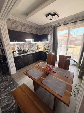 Une cuisine moderne avec des meubles de couleur sombre, un pare-feu en marbre et un coin repas comprenant une table et des bancs en bois.