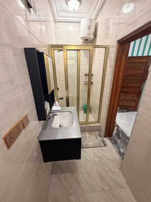 Une salle de bain dotée d’un lavabo moderne, d’une cabine de douche en verre et d’un chauffe-eau apparent.