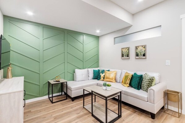 Een moderne woonkamer met een hoekbank, een salontafel en een groene accentmuur.