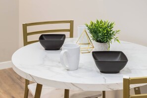 Een ronde marmeren tafel met vier zwarte kommen, een witte mok en een potplant.