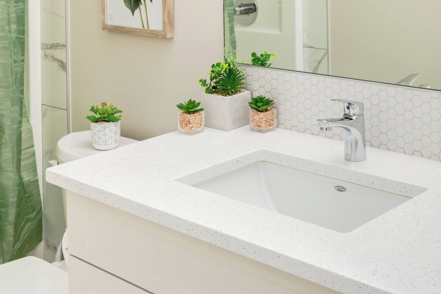 A bathroom with a white sink, a mirror, and three potted plants on the countertop.