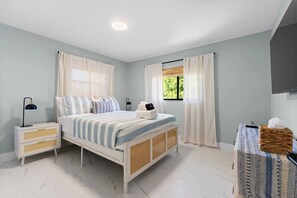 A bedroom with a bed, nightstands, a bedside lamp, a window with curtains, and a wall-mounted TV. - Waterfront Heated Pool | 10 Min to Anna Maria (Bradenton)