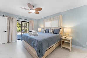 Ein Schlafzimmer mit Bett, Nachttisch mit Lampe, Deckenventilator und Blick durch eine Glastür.
