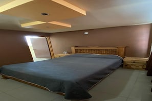 A bedroom with a large bed, a wooden headboard, a nightstand, and a wardrobe.