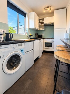 A modern kitchen with built-in appliances, a washing machine, and a bar area. - 3-Bed Bungalow near Elizabeth Line • Parking • Windsor (Slough)
