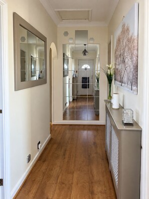 A hallway with a wooden floor, a mirror, a radiator, and a framed picture on the wall. - 3-Bed Bungalow near Elizabeth Line • Parking • Windsor (Slough)
