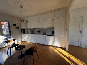 A modern kitchen with white cabinets, a built-in dishwasher, and a dining area with a wooden table and chairs. - Charming Private Apartment in the Heart of København (Copenhagen)