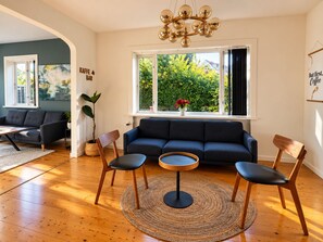 A living room with a dark blue sofa, two wooden chairs, a round coffee table, and a large window with a view of greenery. - Charming Private Apartment in the Heart of København (Copenhagen)