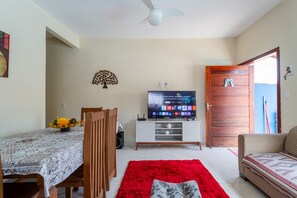 Ein Wohnzimmer mit Fernseher, einem Esstisch mit Stühlen, einem roten Teppich und einer Holztür.