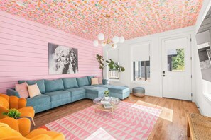 A living room with a pink wall, a blue sofa, a glass coffee table, and a geometric rug. - The Jolene Bubbly Bar with Views 5min to DT (Nashville)