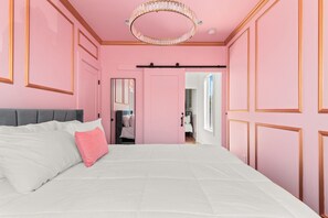Een slaapkamer met een bed, een kroonluchter en roze wanden.