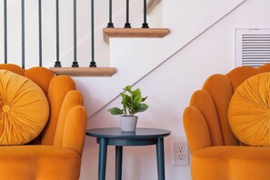 A room with two orange armchairs, a small round table with a potted plant, and a staircase with wooden steps and black railings. - The Jolene Bubbly Bar with Views 5min to DT (Nashville)