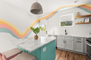 A modern kitchen with a teal island, white cabinets, and a colorful wavy wall design. - The Jolene Bubbly Bar with Views 5min to DT (Nashville)