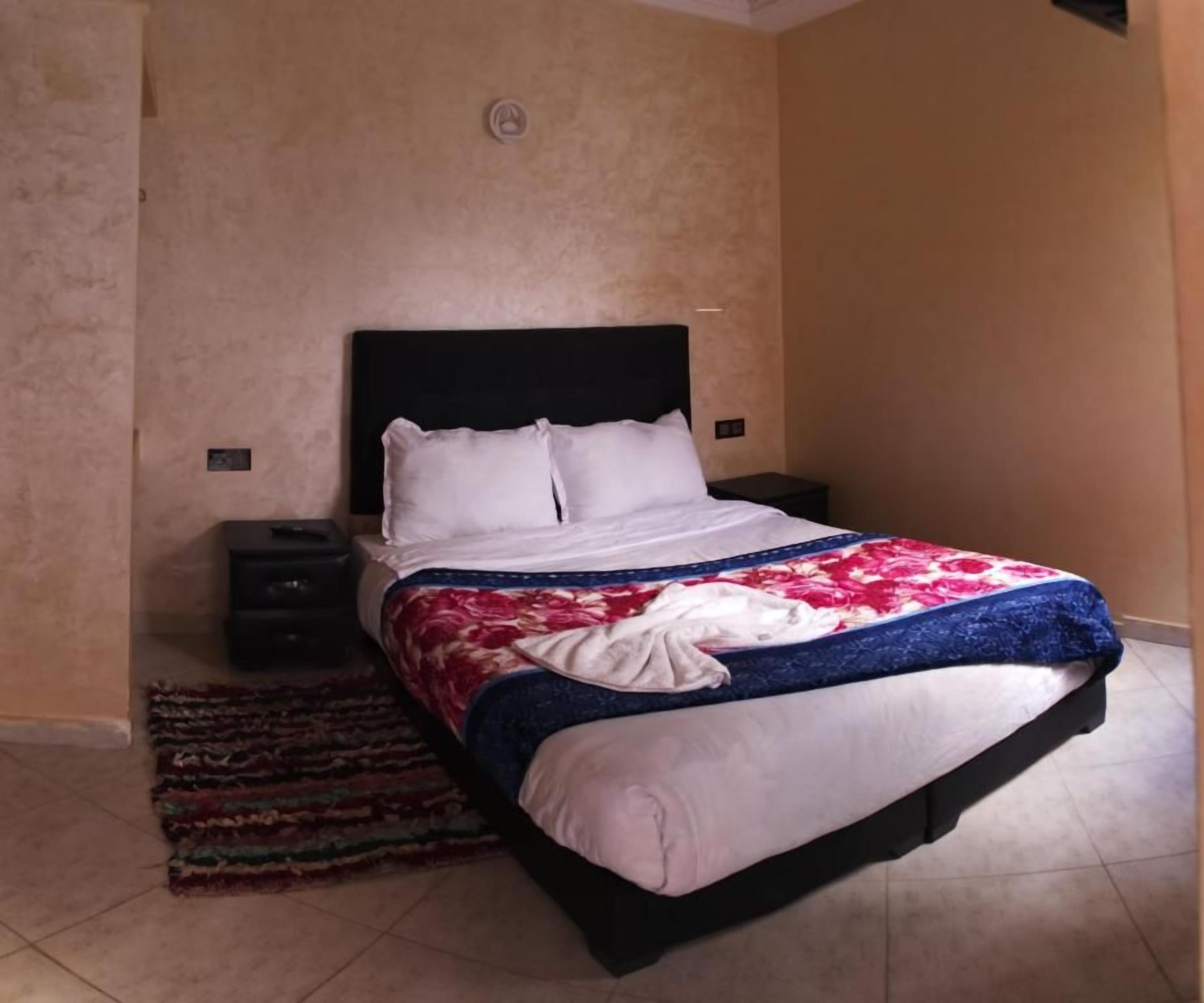 A bedroom with a bed, a nightstand, a rug, and a wall-mounted light.