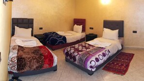 Quarto de hotel com três camas, cada uma com um cobre-cama de padrão diferente.