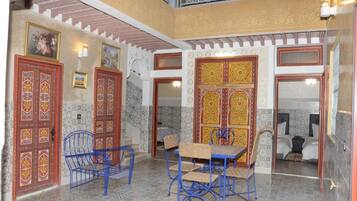 Un interior tradicional con puertas ornamentales, un área de comedor con sillas de metal azul y un dormitorio visible con una cama.