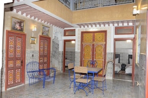Decoração tradicional com portas ornamentadas, área de refeições com cadeiras de metal azuis e um quarto visível com uma cama.