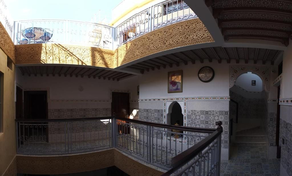 Un interior de varios niveles con intrincados trabajos de azulejos, un balcón con barandilla de hierro forjado y una escalera que conduce a un nivel superior.