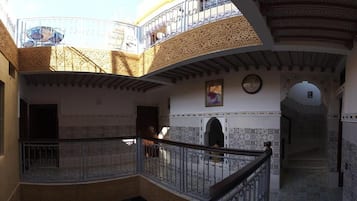 Un interior de varios niveles con intrincados trabajos de azulejos, un balcón con barandilla de hierro forjado y una escalera que conduce a un nivel superior.