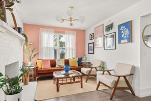 Ein Wohnzimmer mit Kamin aus weißem Mauerwerk, einem braunen Sofa mit Kissen, einem Glastisch und einem Holzstuhl.