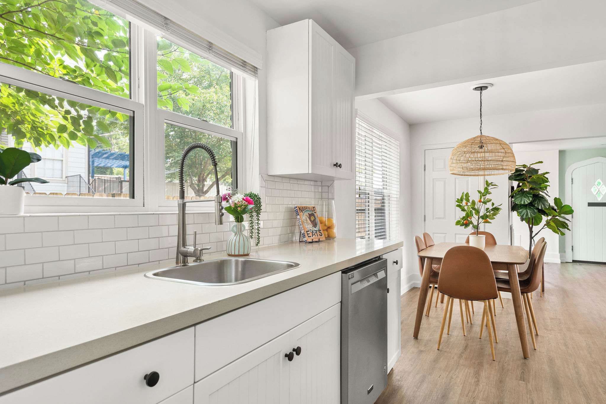 A modern kitchen with white cabinetry, a stainless steel sink, and a dining area with a wooden table and chairs.