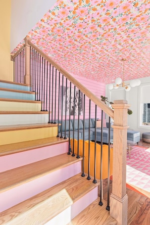 Eine Treppe mit Holzdielen und schwarzen Geländern, die zu einem Raum mit einer floralen Decke und einem blauen Sofa führt.