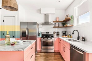 A modern kitchen with pink cabinets, stainless steel appliances, and a white countertop. - Dollys Dream House Champagne Bar w DT views (Nashville)