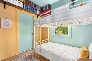 A bunk bed room with a bookshelf, a door, and a window with a view of trees. - Dollys Dream House Champagne Bar w DT views (Nashville)