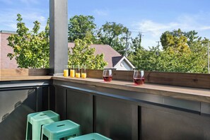 A balcony with a wooden railing, two green stools, and three glasses of beverages. - Dollys Dream House Champagne Bar w DT views (Nashville)