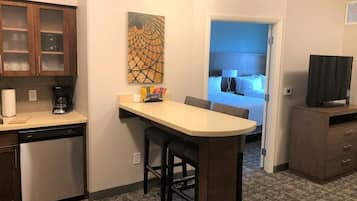 A compact kitchen with a dishwasher, a coffee maker, and a small bar area with stools.