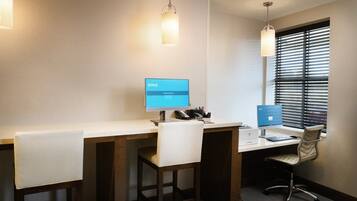 A hotel room with a desk, two chairs, a computer, and a window with blinds.