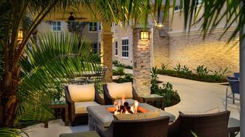 An outdoor patio area with wicker furniture, a fire pit, and palm trees.