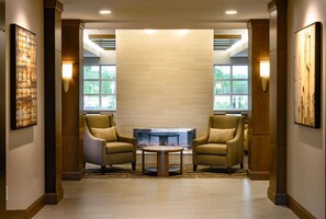Un hall d’entrée avec deux fauteuils, une table basse, une cheminée et de grandes fenêtres.