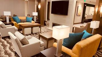 A hotel lobby with a sofa, armchairs, a TV, and a fireplace.