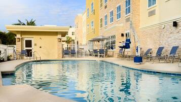 A swimming pool with lounge chairs, a covered seating area, and a building with multiple windows.